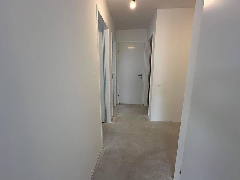 Heller Flur mit weißen Wänden und Betonboden, der zu verschiedenen Räumen der Wohnung führt.