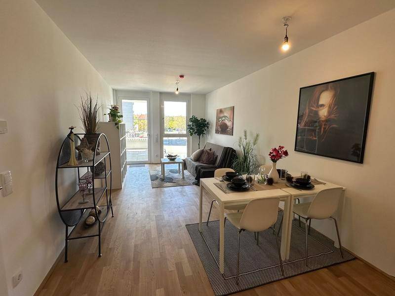 Freundlicher Wohn- und Essbereich mit Holzboden und Zugang zum Balkon.
