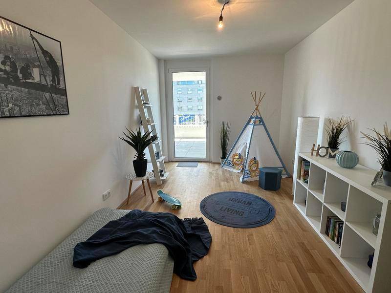 Helles Kinder- oder Gästezimmer mit Holzboden und Zugang zu einem Außenbereich.