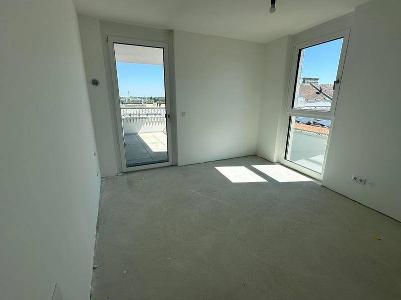 Heller, unmöblierter Raum mit Rohbetonboden und Zugang zu einem Balkon oder einer Terrasse.