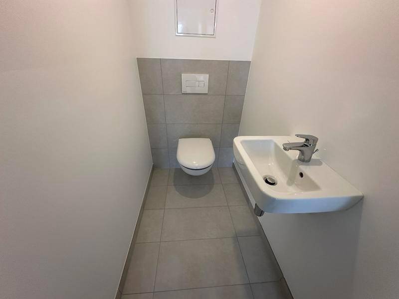 Kompaktes Gäste-WC mit modernen grauen Fliesen, wandhängendem WC und kleinem Waschbecken.