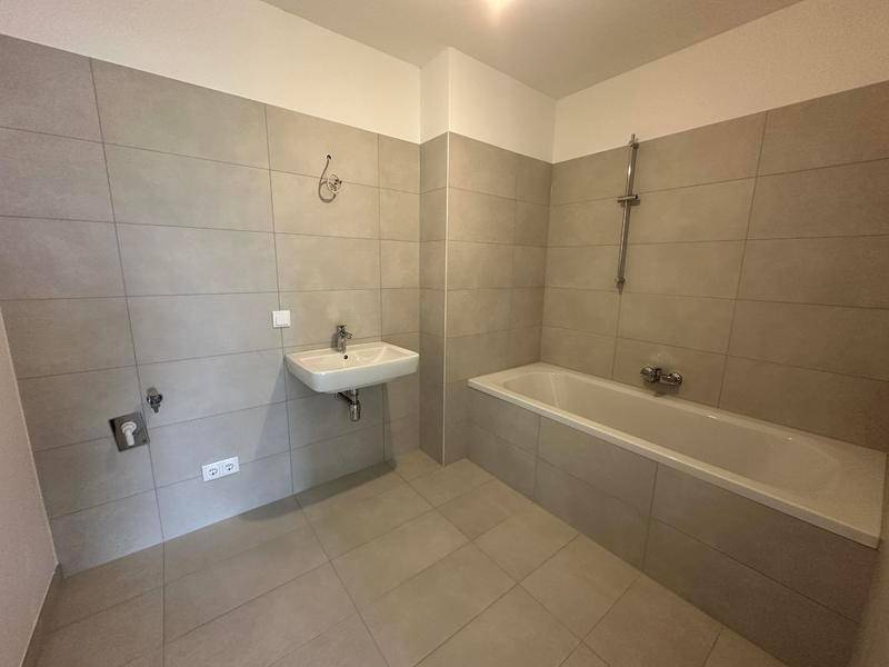 Modernes Badezimmer mit grauen Fliesen, einer Badewanne und einem einzelnen Waschbecken.
