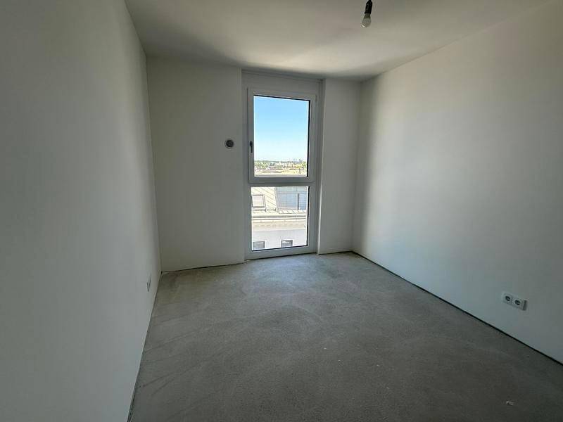 Heller, unmöblierter Raum mit Rohbetonboden und einem hohen Fenster, ideal für ein Schlafzimmer.