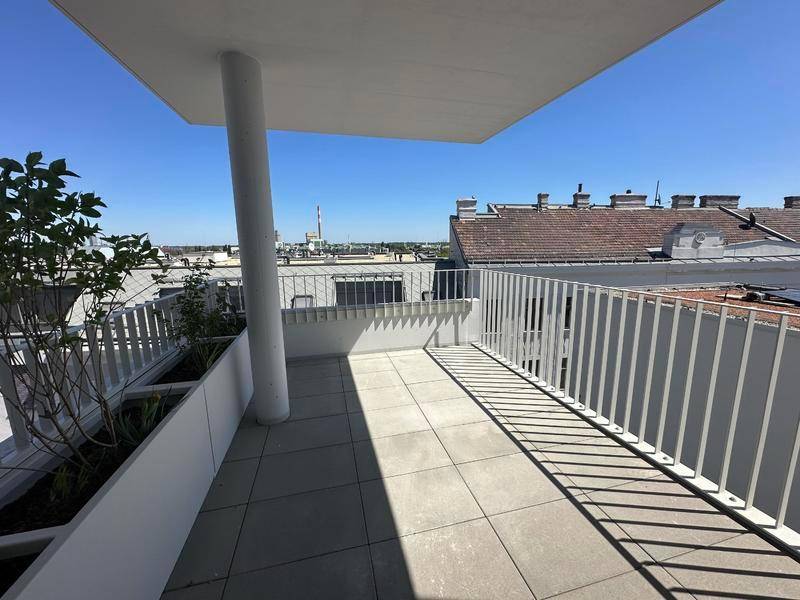 Sonniger Außenbereich mit Fliesenboden, modernen Geländern und Blick über die Dächer der Stadt.