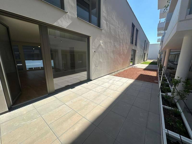 Moderne Terrasse mit Fliesenboden und Zugang zu einem hellen Innenraum, umgeben von Neubauten.