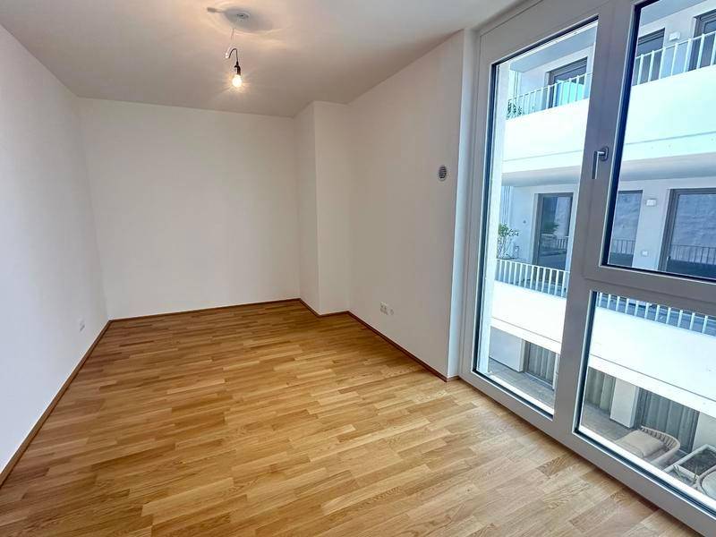 Leeres Schlafzimmer mit Parkettboden und bodentiefen Fenstern, die einen Blick nach draußen bieten.