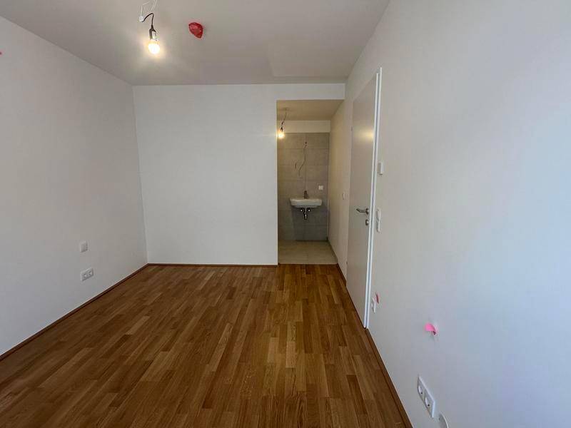 Helles Zimmer mit Parkettboden und angrenzendem Badezimmer, ideal als Schlaf- oder Gästezimmer.