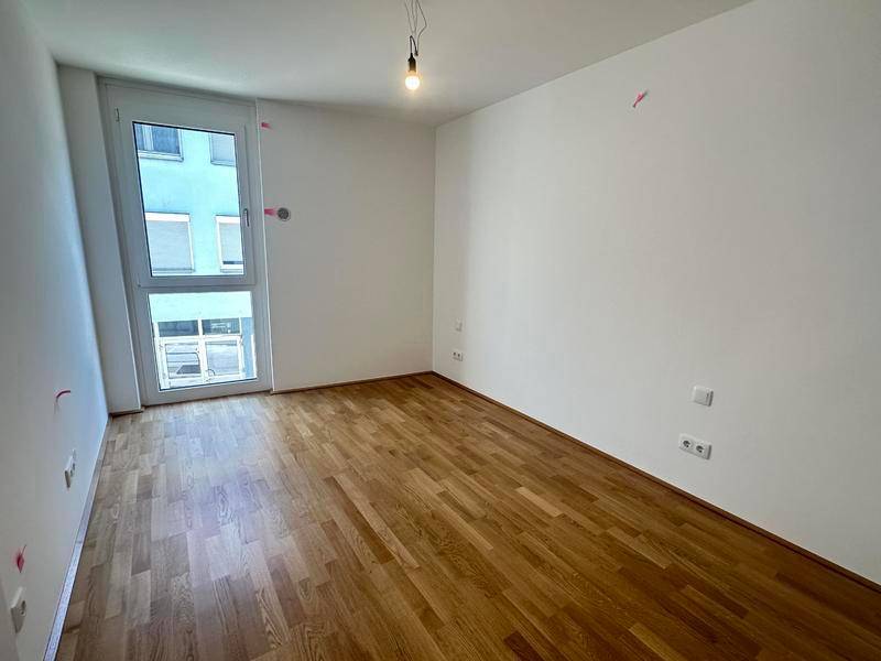 Leeres Zimmer mit Parkettboden und einem großen Fenster, das viel Licht in den Raum bringt.