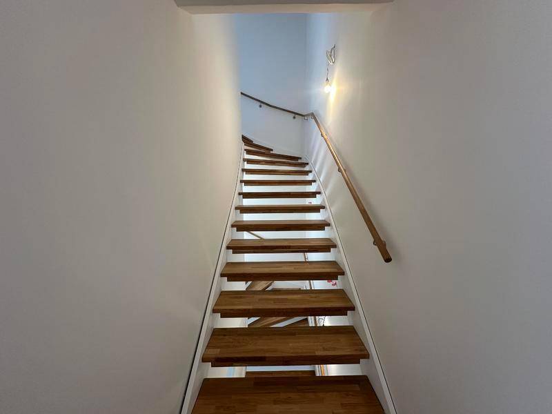 Holztreppe mit Handlauf in einem hellen Treppenhaus, das die Etagen miteinander verbindet.