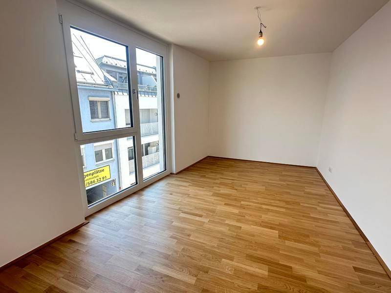 Helles Zimmer mit Parkettboden und großem Fenster, das einen Blick auf die Umgebung ermöglicht.