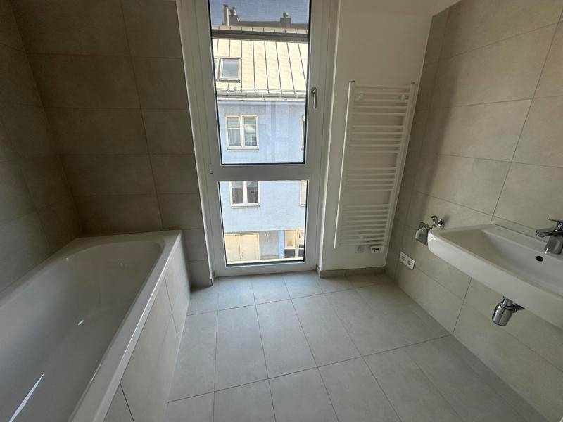 Modernes Badezimmer mit Badewanne, Waschbecken und beheiztem Handtuchhalter, hell gefliest.