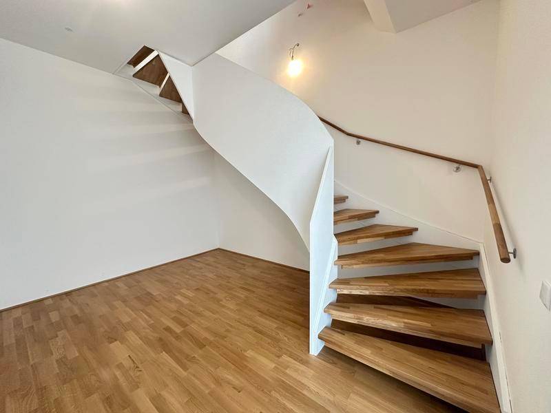 Elegante Wendeltreppe aus Holz mit weißer Brüstung, die die verschiedenen Ebenen verbindet.