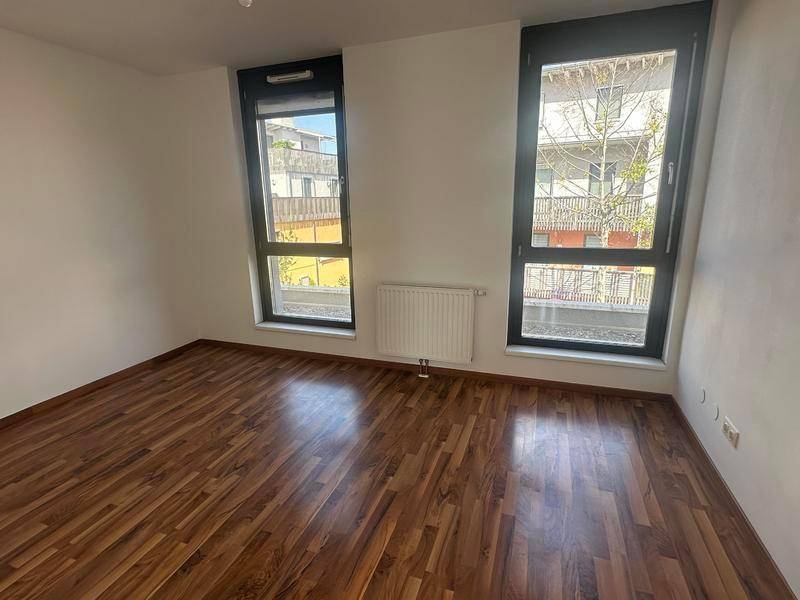 Helles Schlafzimmer mit Holzboden und zwei großen Fenstern, die den Raum erhellen.