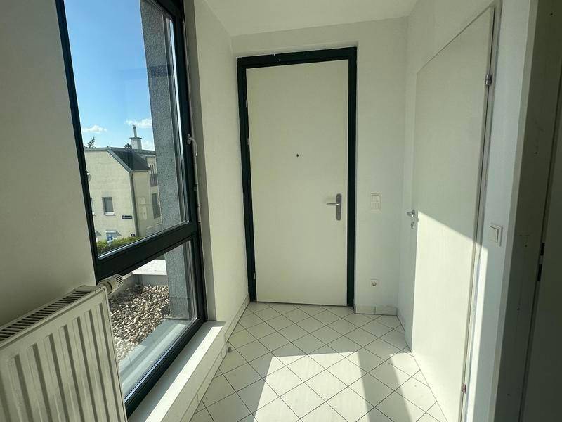 Eingangsbereich mit Fliesenboden, großer Fenstertür und Heizkörper, der viel Licht spendet.