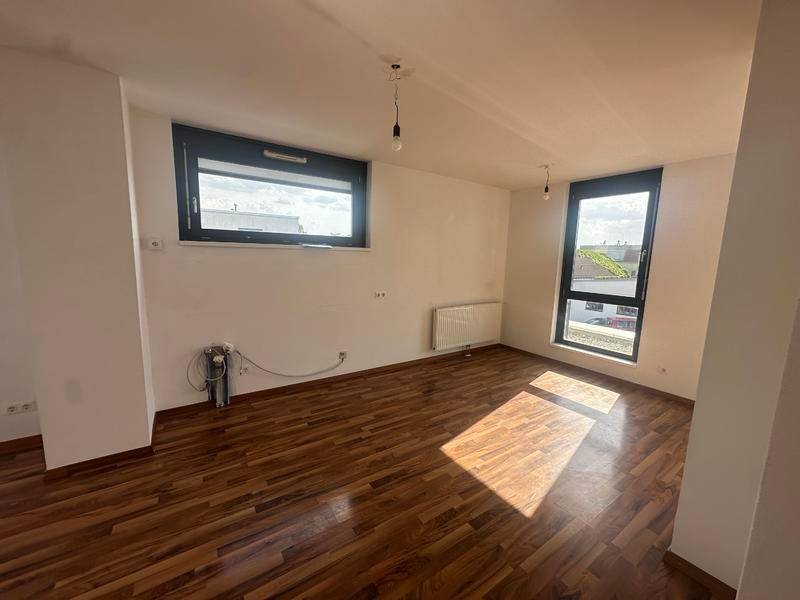 Lichtdurchflutetes Wohnzimmer mit Holzboden und großen Fenstern, die viel Tageslicht hereinlassen.