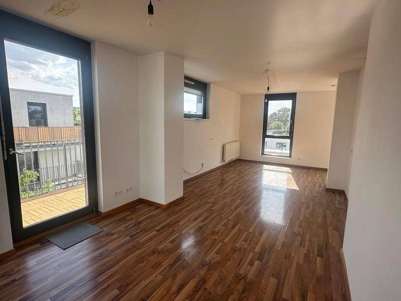 Helles Wohnzimmer mit Holzboden und Zugang zu einem Balkon, durchflutet von Sonnenlicht.