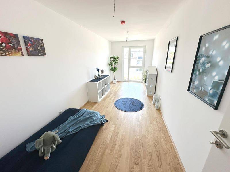 Helles Schlafzimmer mit Holzboden, weiß gestrichenen Wänden und Zugang nach draußen.