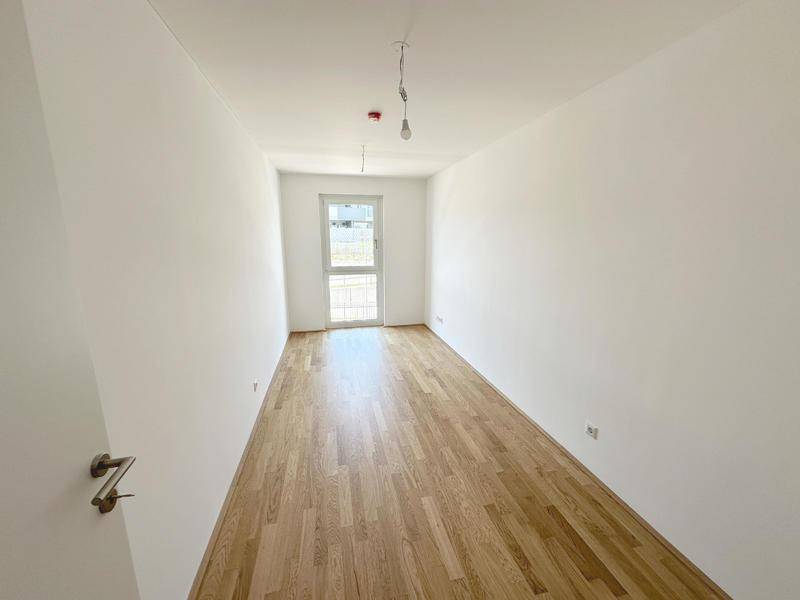 Freundliches, leeres Zimmer mit Parkettboden und viel Tageslicht durch das Fenster.