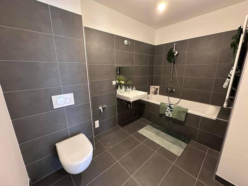 Modernes Badezimmer mit dunklen Fliesen, Badewanne und wandhängendem WC.