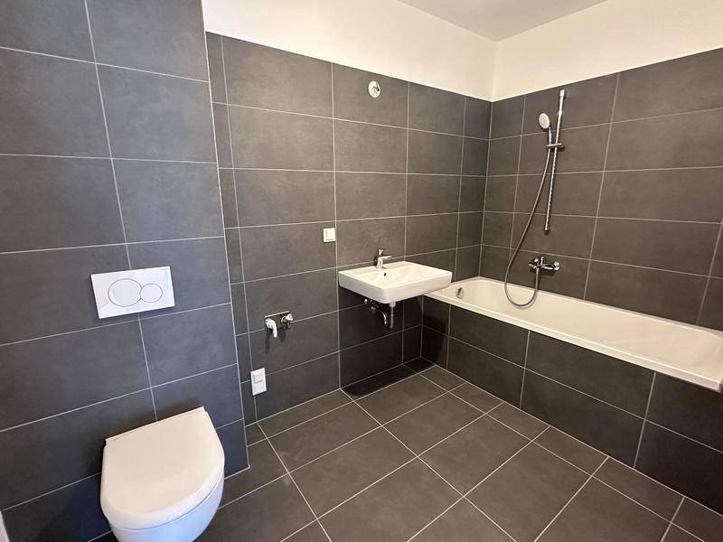 Modernes Badezimmer mit dunkelgrauen Fliesen, Badewanne mit Duschfunktion, WC und Waschbecken.