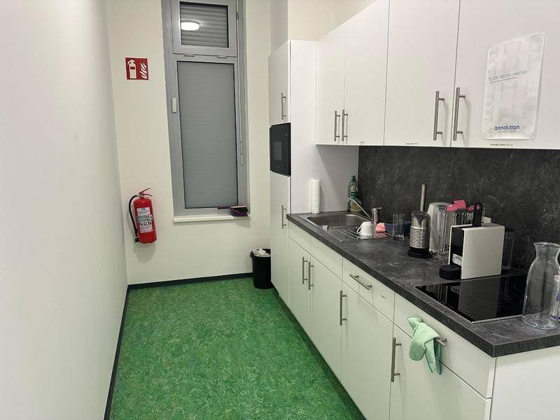 Funktionale Teeküche mit weißen Schränken, dunkler Arbeitsplatte und grünem Linoleumboden.