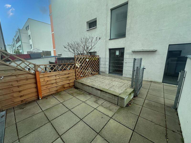 Gepflasterte Terrasse im Freien mit Holzzaun und Metallgitter, bietet privaten Außenbereich.