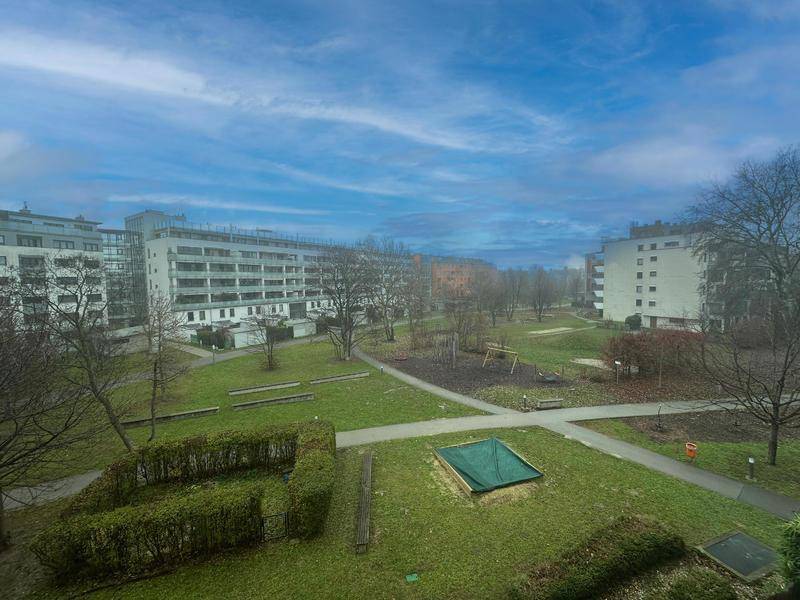Weitläufige Grünanlage mit Spielplatz und Wohngebäuden im Hintergrund unter blauem Himmel.