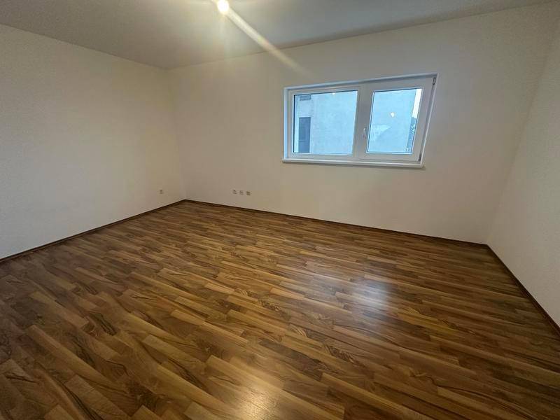 Leeres Schlafzimmer mit Laminatboden und einem großen Fenster, das viel Tageslicht hereinlässt.