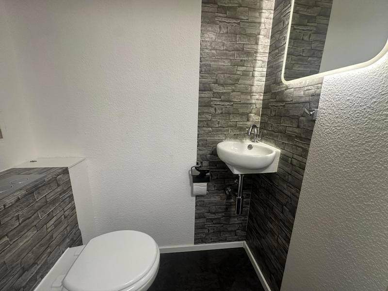 Modernes Gäste-WC mit Wand-WC, kleinem Waschbecken und dekorativer Steinoptik-Wand.