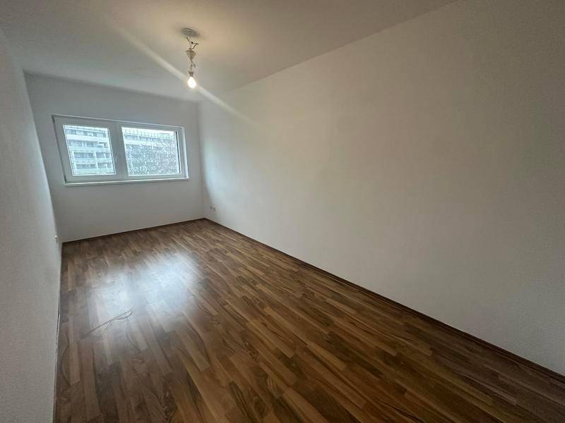 Geräumiges, leeres Zimmer mit Laminatboden und Fenster, bereit für individuelle Gestaltung.