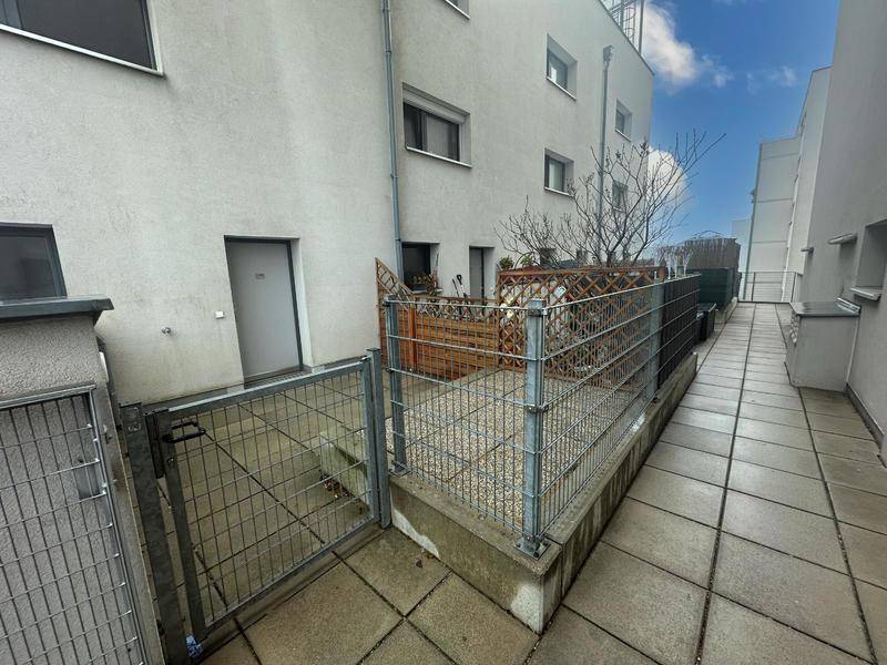 Außenbereich mit gepflasterter Terrasse und Zugangsweg, umgeben von Metallzäunen.