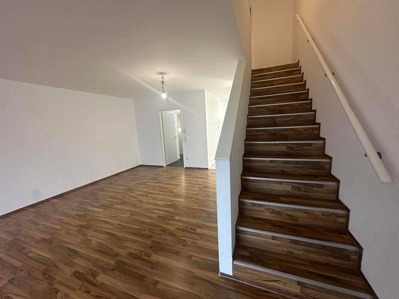Heller Eingangsbereich mit Holztreppe und Laminatboden, der zu den oberen Etagen führt.
