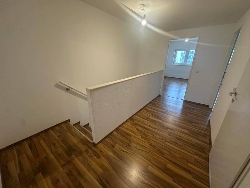 Oberer Flur mit Laminatboden und Treppengeländer, der zu weiteren Räumen führt.