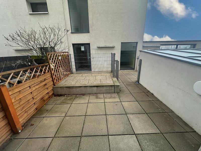 Geräumige gepflasterte Terrasse mit Holzzaun und Zugang zum Gebäude, ideal für Entspannung.