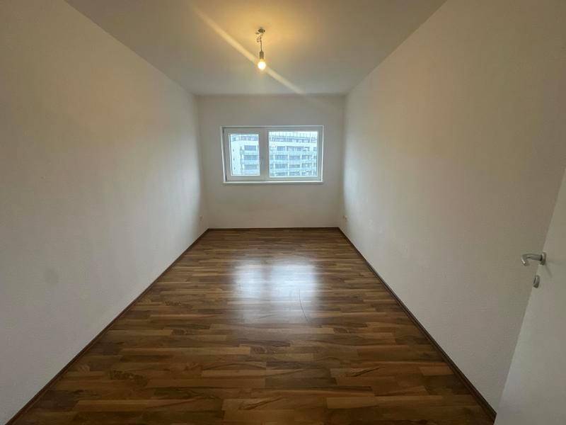 Helles, leeres Zimmer mit Laminatboden und Fenster, das sich gut als Schlaf- oder Arbeitszimmer eignet.