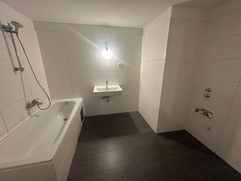 Badezimmer mit Badewanne, Duschbereich und Waschbecken, ausgestattet mit dunklen Bodenfliesen.