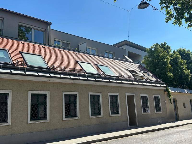 Historisches Gebäude mit Satteldach und mehreren Dachfenstern, daneben moderne Architektur.