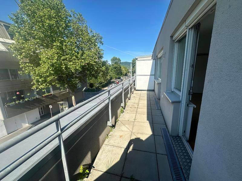 Langer Balkon mit Fliesenboden und Blick auf die Straße und umliegende Gebäude.