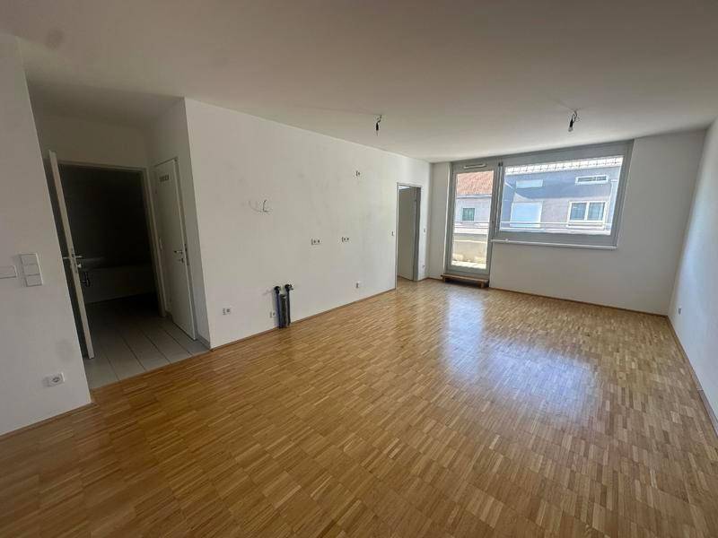 Geräumiges, leeres Zimmer mit Parkettboden und viel Tageslicht, ideal für Wohn- oder Schlafbereich.