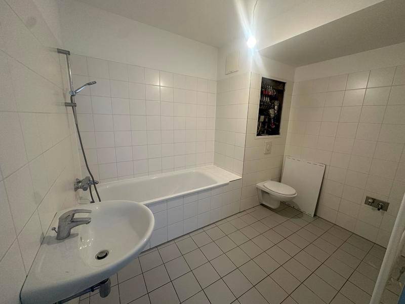 Badezimmer mit weißen Fliesen, Badewanne mit Duschfunktion und einem Waschbecken.