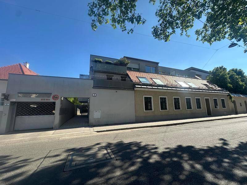 Ansicht eines historischen Gebäudes mit moderner Erweiterung und Garagenzufahrt an einer Straße.