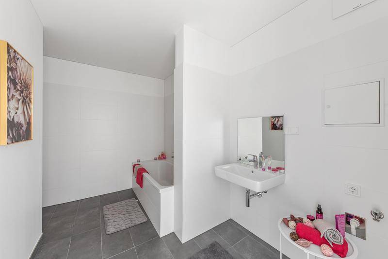 Helles Badezimmer mit Badewanne, Einzelwaschbecken und modernen grauen Fliesen am Boden.