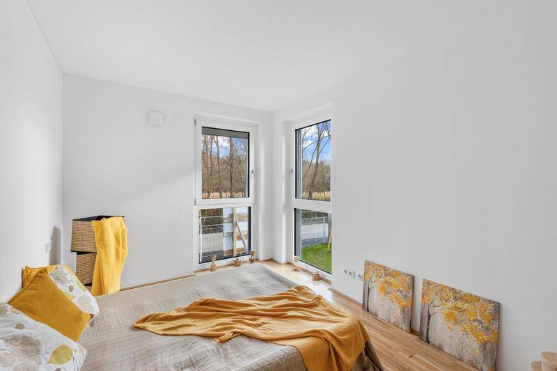 Schlafzimmer mit Holzboden und zwei Fenstern, die einen schönen Blick ins Grüne bieten.