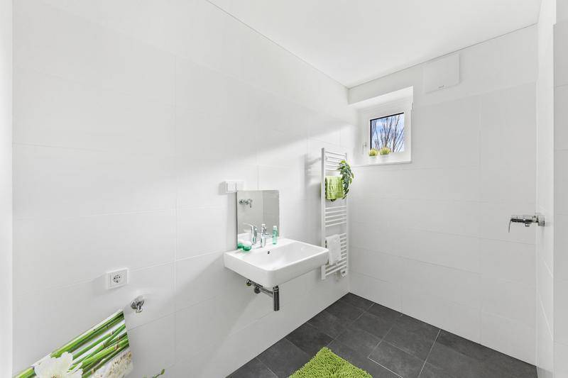 Helles Badezimmer mit Dusche, Einzelwaschbecken, Fenster und beheiztem Handtuchhalter.