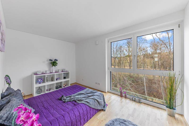 Geräumiges Schlafzimmer mit Holzboden und einem großen Fenster mit weitem Blick ins Grüne.