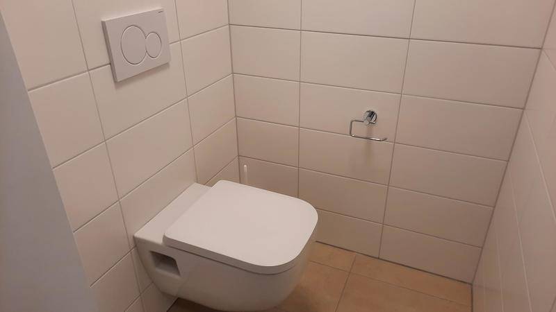 Modern gefliestes Gäste-WC mit wandhängender Toilette und schlichtem Design.