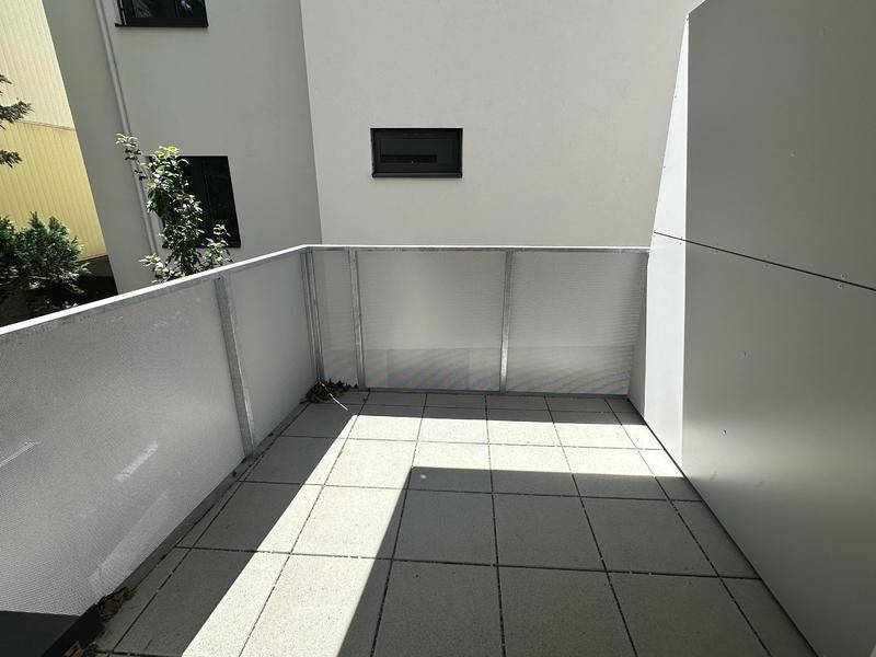 Kleiner, gefliester Balkon mit weißer Brüstung und viel Sonnenlicht.