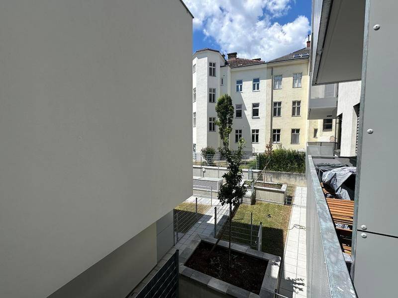 Blick vom Balkon auf den begrünten Innenhof mit jungen Bäumen und angrenzenden Gebäuden.
