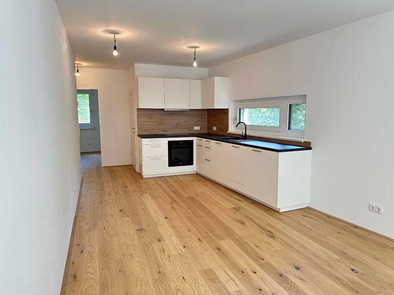 Moderne Einbauküche in L-Form mit dunkler Arbeitsplatte und hellem Holzboden im offenen Wohnbereich.