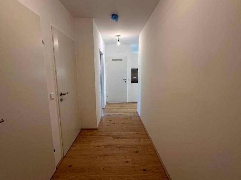 Langer, heller Flur mit Holzboden und mehreren weißen Türen, der zu den Zimmern führt.